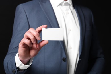 Photo of Businessman holding blank business card on black background, closeup