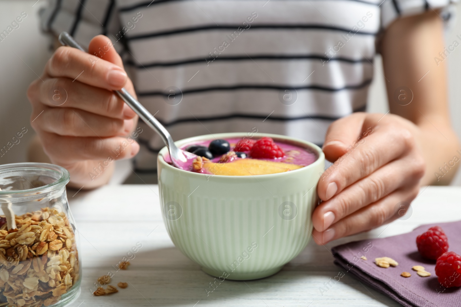 Photo of Woman eating tasty acai smoothie with fruits at white wooden table, closeup