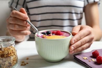 Woman eating tasty acai smoothie with fruits at white wooden table, closeup