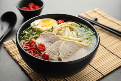 Photo of Delicious ramen with meat in bowl served on grey table, closeup. Noodle soup