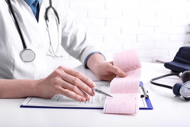 Photo of Doctor examining cardiogram at table in clinic, closeup