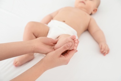 Mother and her cute child on white bed, closeup. Baby massage and exercises