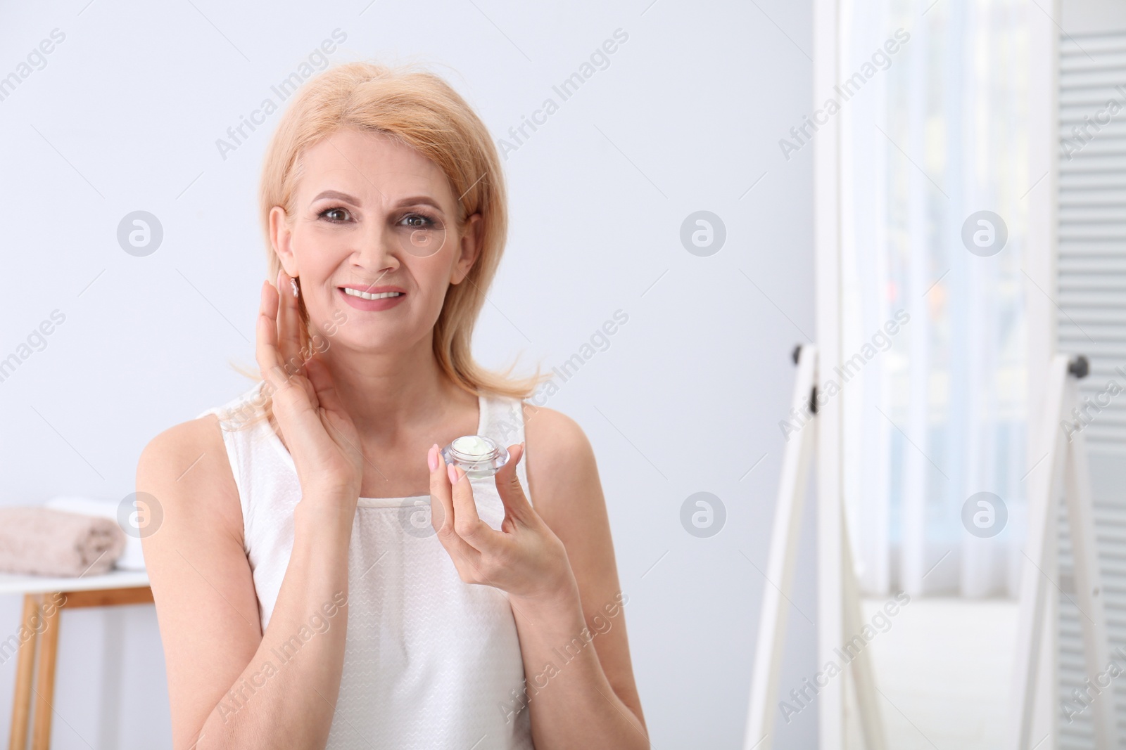 Photo of Mature woman applying face cream at home. Space for text