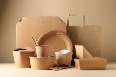 Photo of Eco friendly food packaging. Paper containers, tableware and bag on white table against beige background