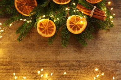 Photo of Flat lay composition with dry orange slices, cinnamon sticks, fir branches and Christmas lights on wooden table. Space for text
