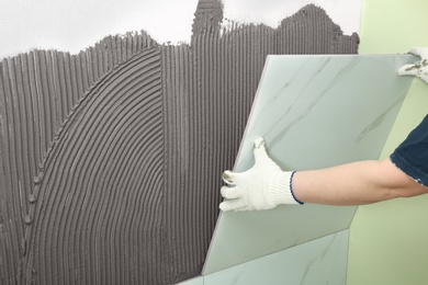 Worker installing ceramic tile on wall, closeup. Space for text