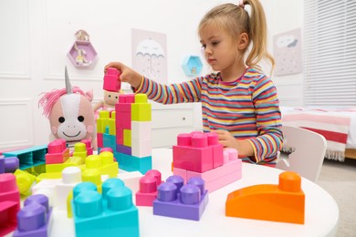 Photo of Cute little girl playing with colorful building blocks at table in room