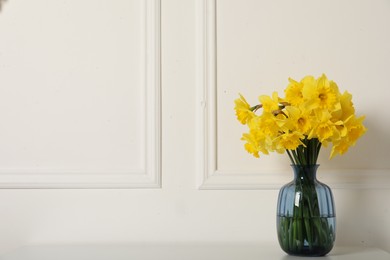 Beautiful daffodils in vase on table near white wall indoors, space for text