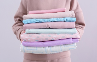 Photo of Woman holding stack of clean bed linens on light background, closeup