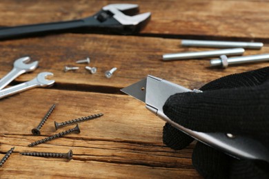 Man holding utility knife and different tools on wooden table, closeup