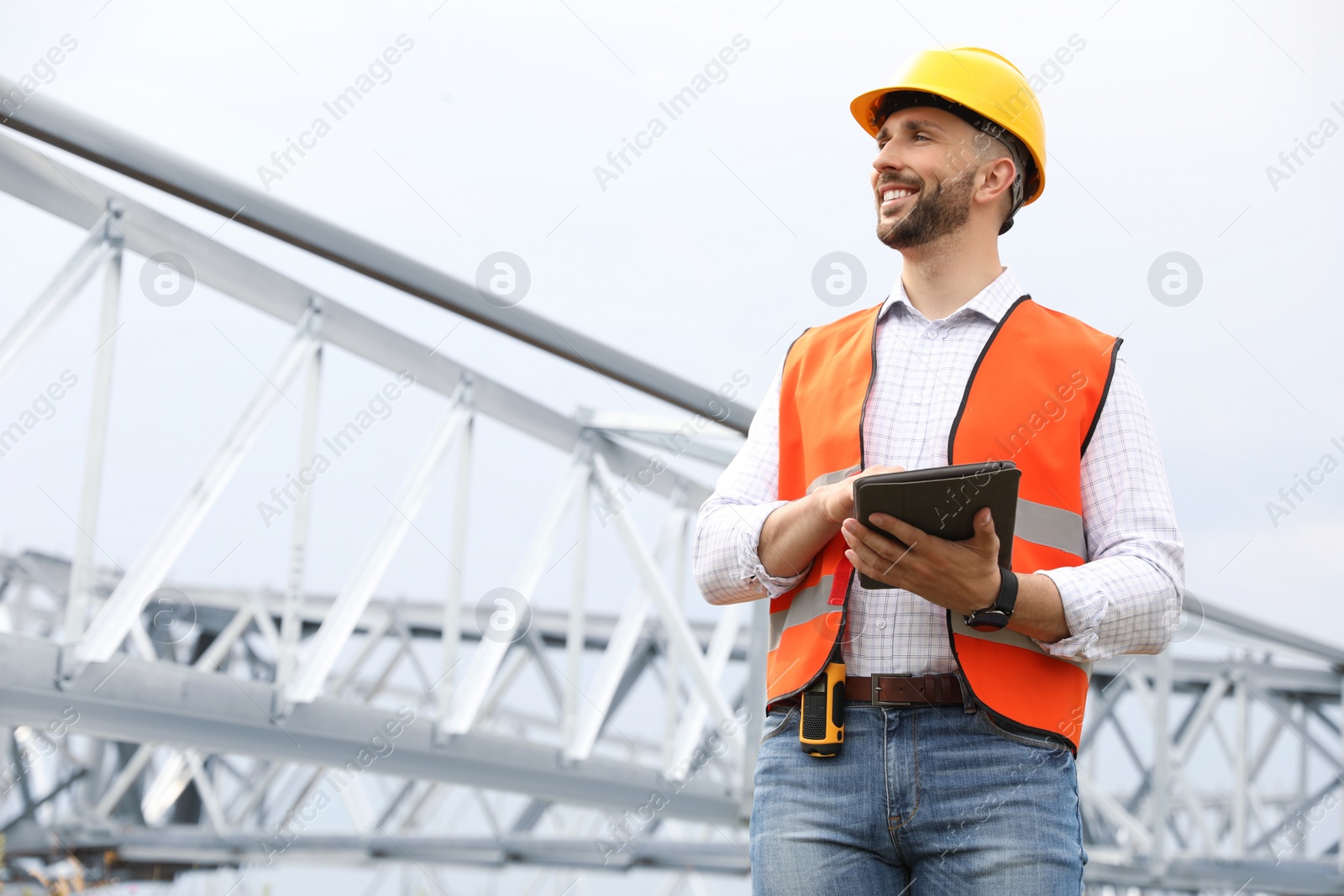 Photo of Professional engineer with tablet near high voltage tower construction outdoors. Installation of electrical substation