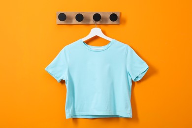 Photo of Hanger with light blue T-shirt on orange wall