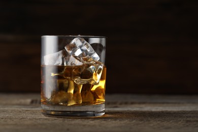 Photo of Whiskey with ice cubes in glass on wooden table, closeup. Space for text