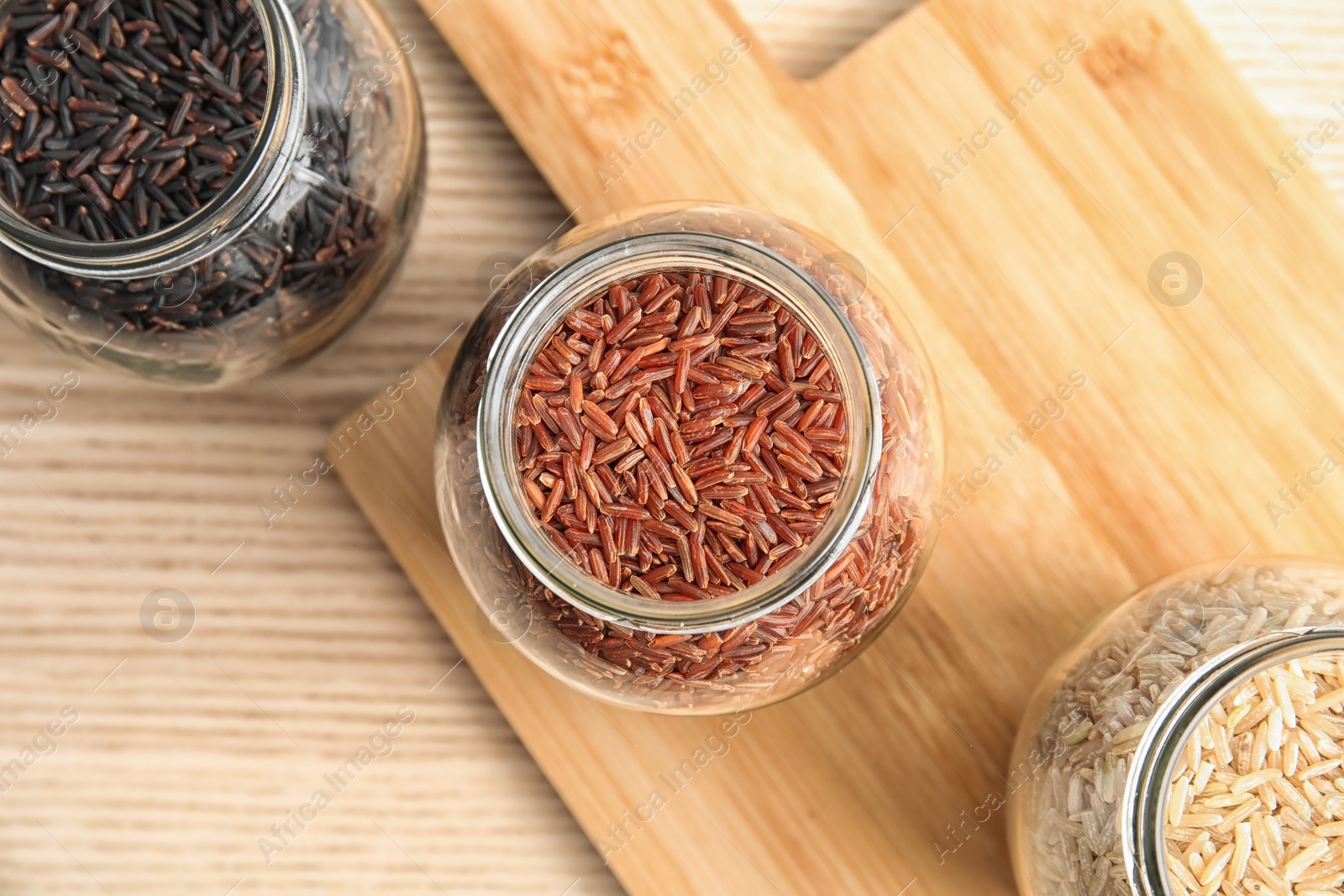 Photo of Jars with different types of rice and board on wooden table, top view