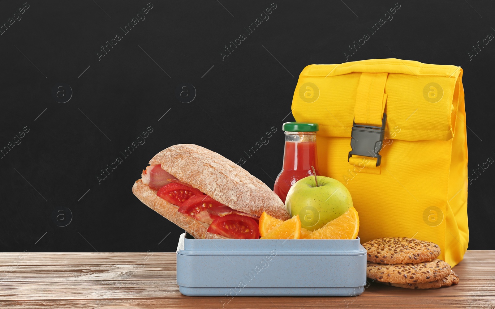 Image of Lunch box with appetizing food and bag on wooden table near blackboard