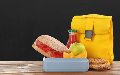 Lunch box with appetizing food and bag on wooden table near blackboard