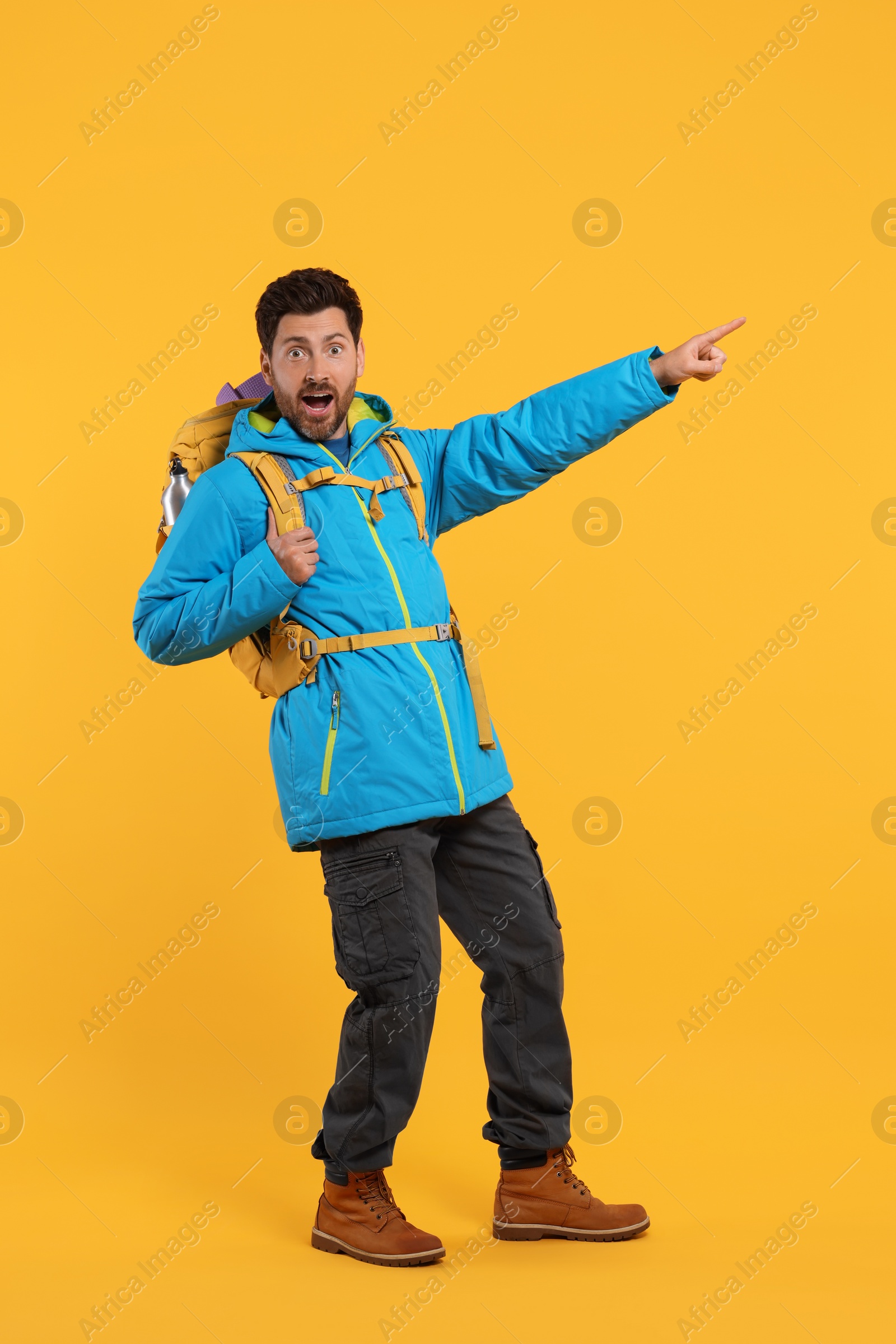 Photo of Emotional man with backpack pointing at something on orange background. Active tourism