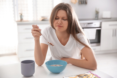 Sleepy young woman eating breakfast at home in morning