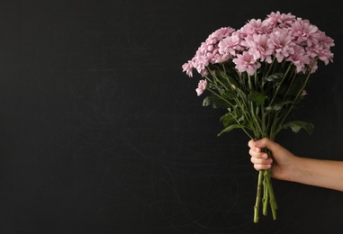 Photo of Woman holding beautiful bouquet near black chalkboard, space for text. Happy Teacher's Day