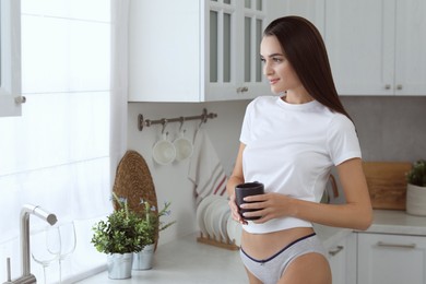 Photo of Young woman with cup wearing white t-shirt and comfortable underwear indoors. Space for text