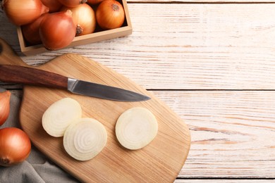 Photo of Whole and sliced onions on white wooden table, flat lay. Space for text