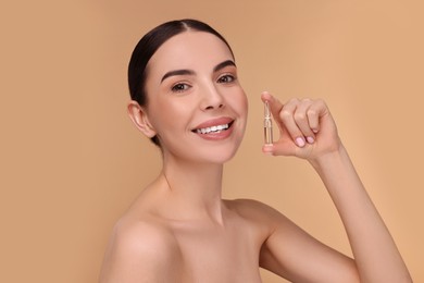 Beautiful young woman holding skincare ampoule on beige background