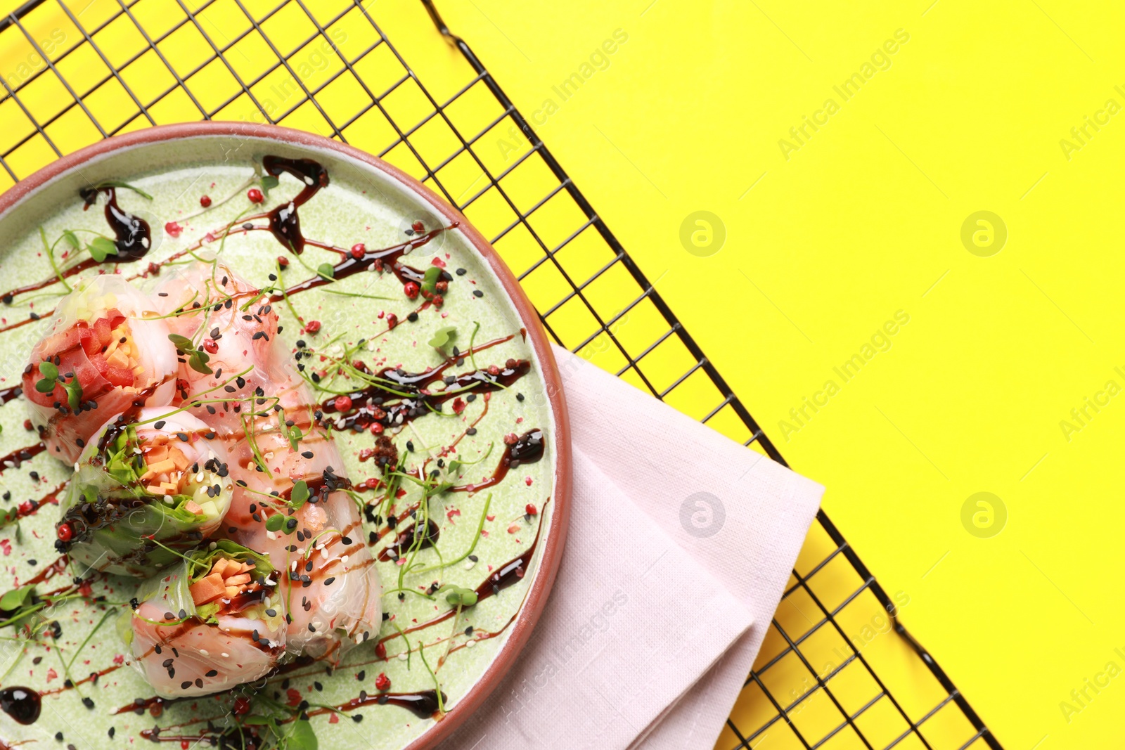 Photo of Delicious spring rolls with sauce and microgreens on yellow background, top view. Space for text