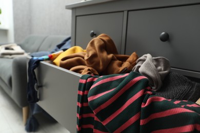 Cluttered chest of drawers indoors, closeup. Clothes in mess