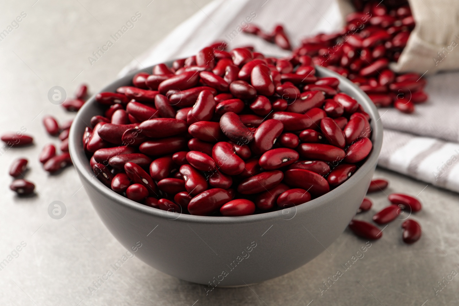 Photo of Raw red kidney beans in bowl on light grey table, closeup