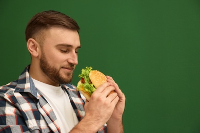 Photo of Young man eating tasty burger on color background. Space for text