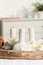 Photo of Wicker tray with herbal bags and other spa products on white bath towel