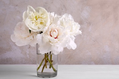 Photo of Beautiful peonies in glass vase on white table. Space for text