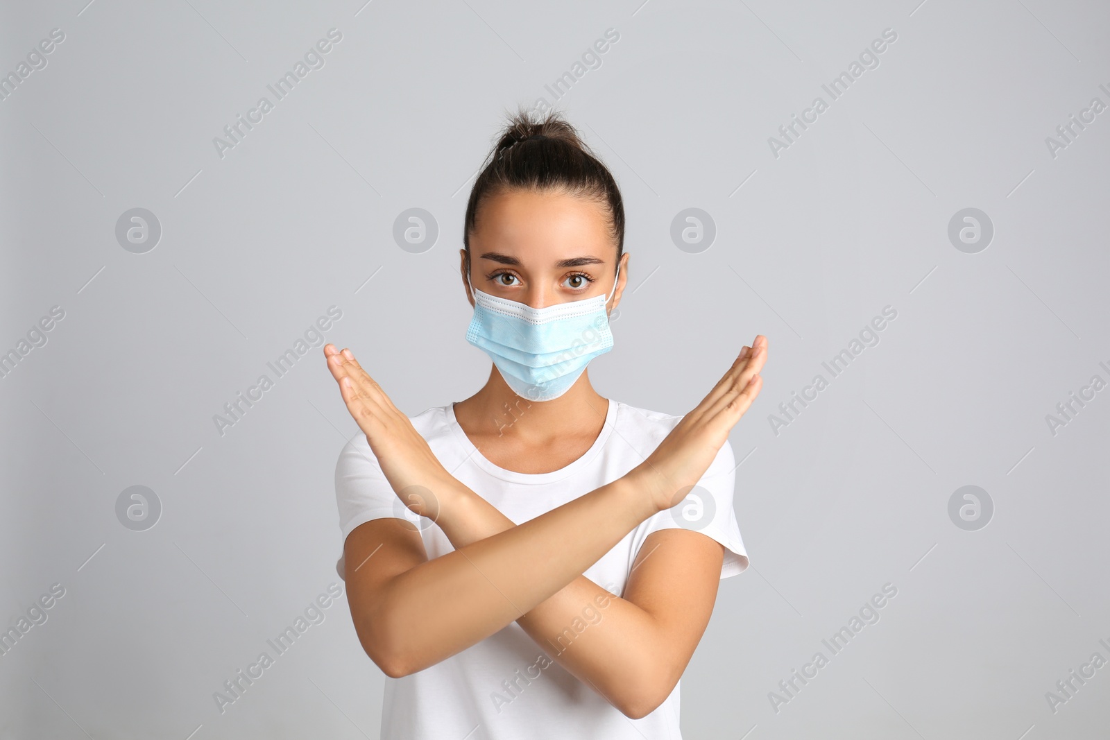 Photo of Woman in protective mask showing stop gesture on grey background. Prevent spreading of COVID‑19