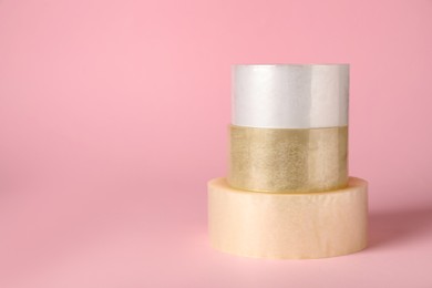 Photo of Three rolls of adhesive tape on pink background. Space for text