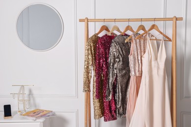 Rack with collection of stylish dresses near mirror in room. Preparing for party