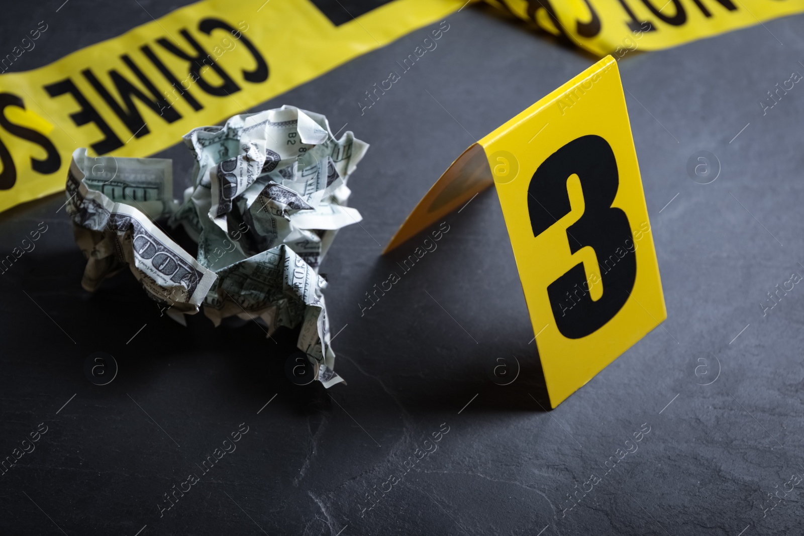 Photo of Crime scene marker and crumpled dollars on black slate table, closeup