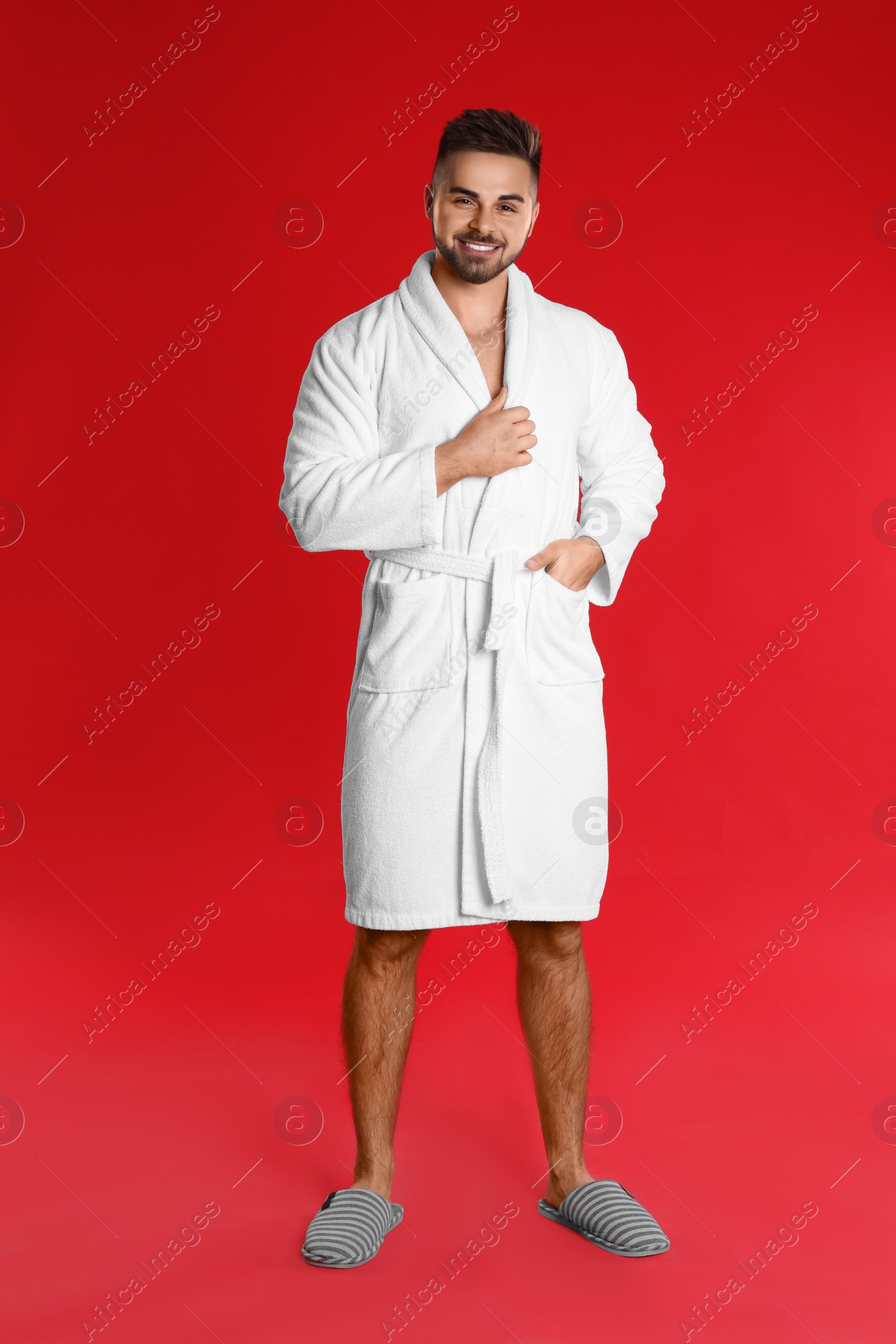 Photo of Happy young man in bathrobe on red background