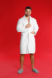 Photo of Happy young man in bathrobe on red background