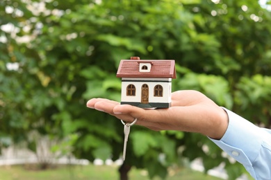 Photo of Real estate agent holding house model and key on blurred background