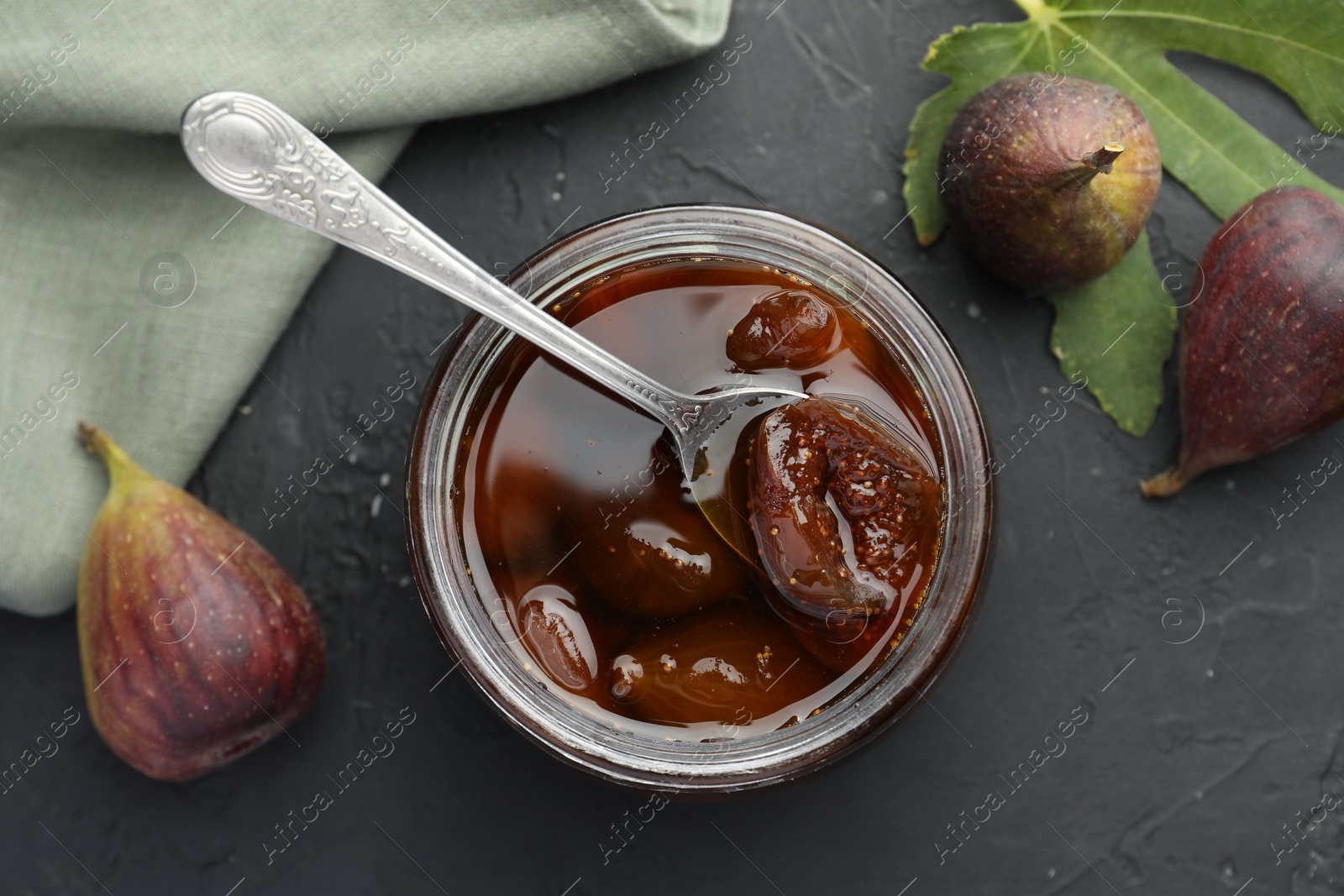 Photo of Jar of tasty sweet jam and fresh figs on black table, flat lay