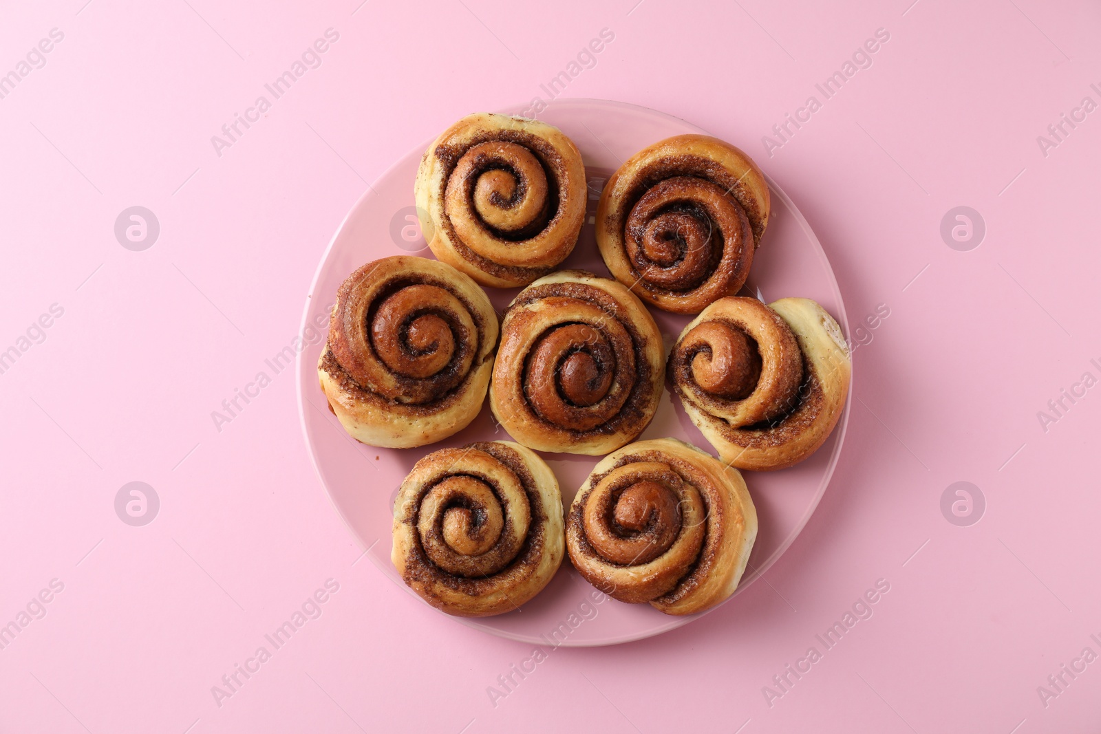 Photo of Many tasty cinnamon rolls pink background, top view