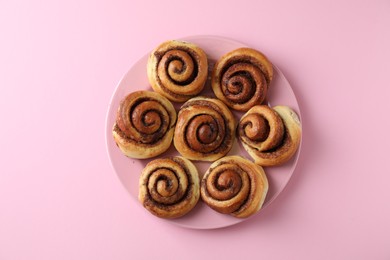 Many tasty cinnamon rolls pink background, top view