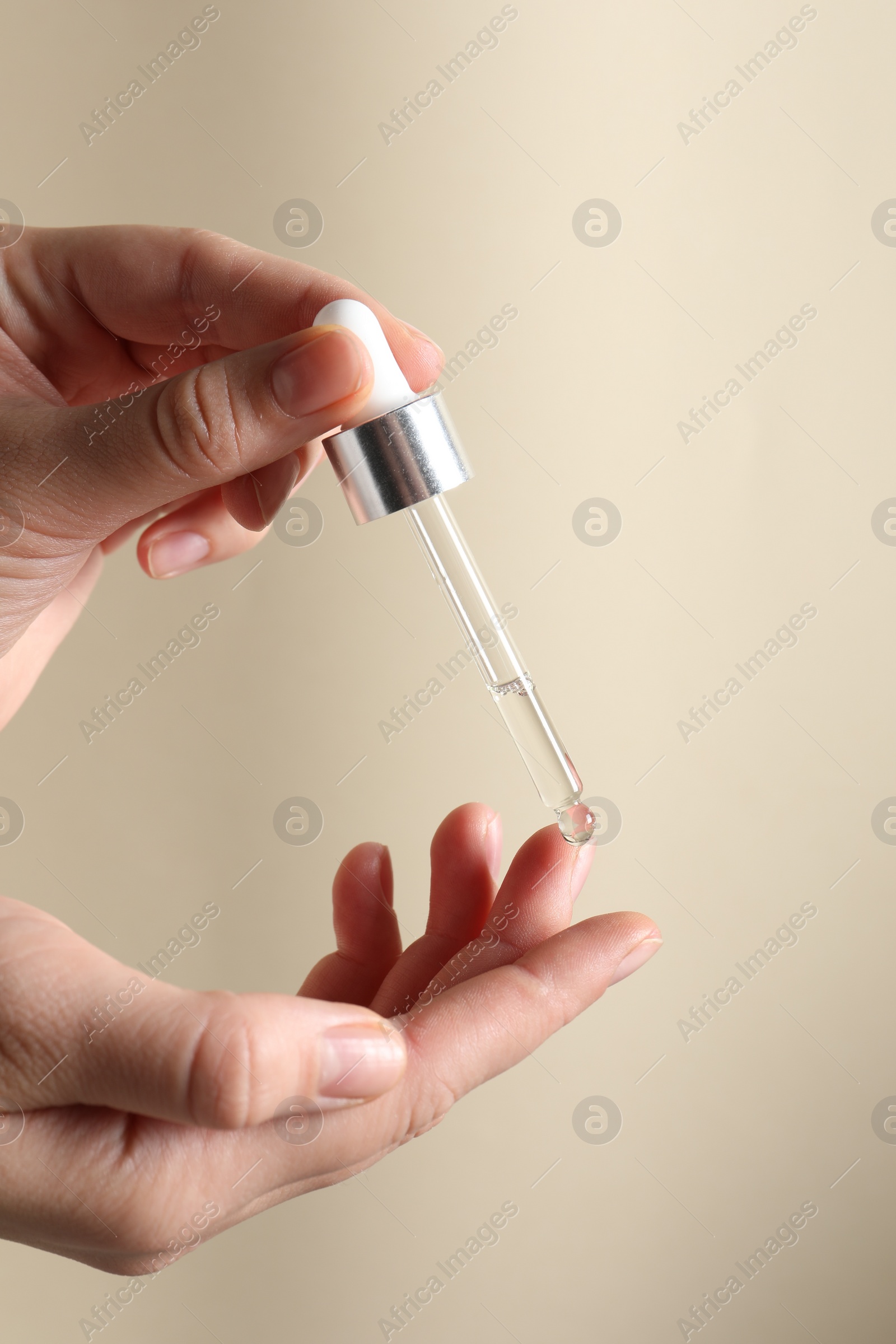 Photo of Woman applying cosmetic serum onto finger on beige background, closeup