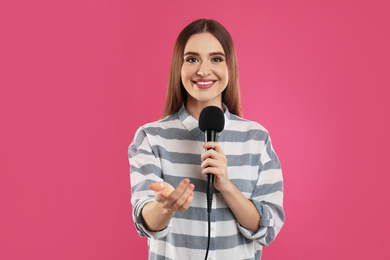 Photo of Young female journalist with microphone on pink background