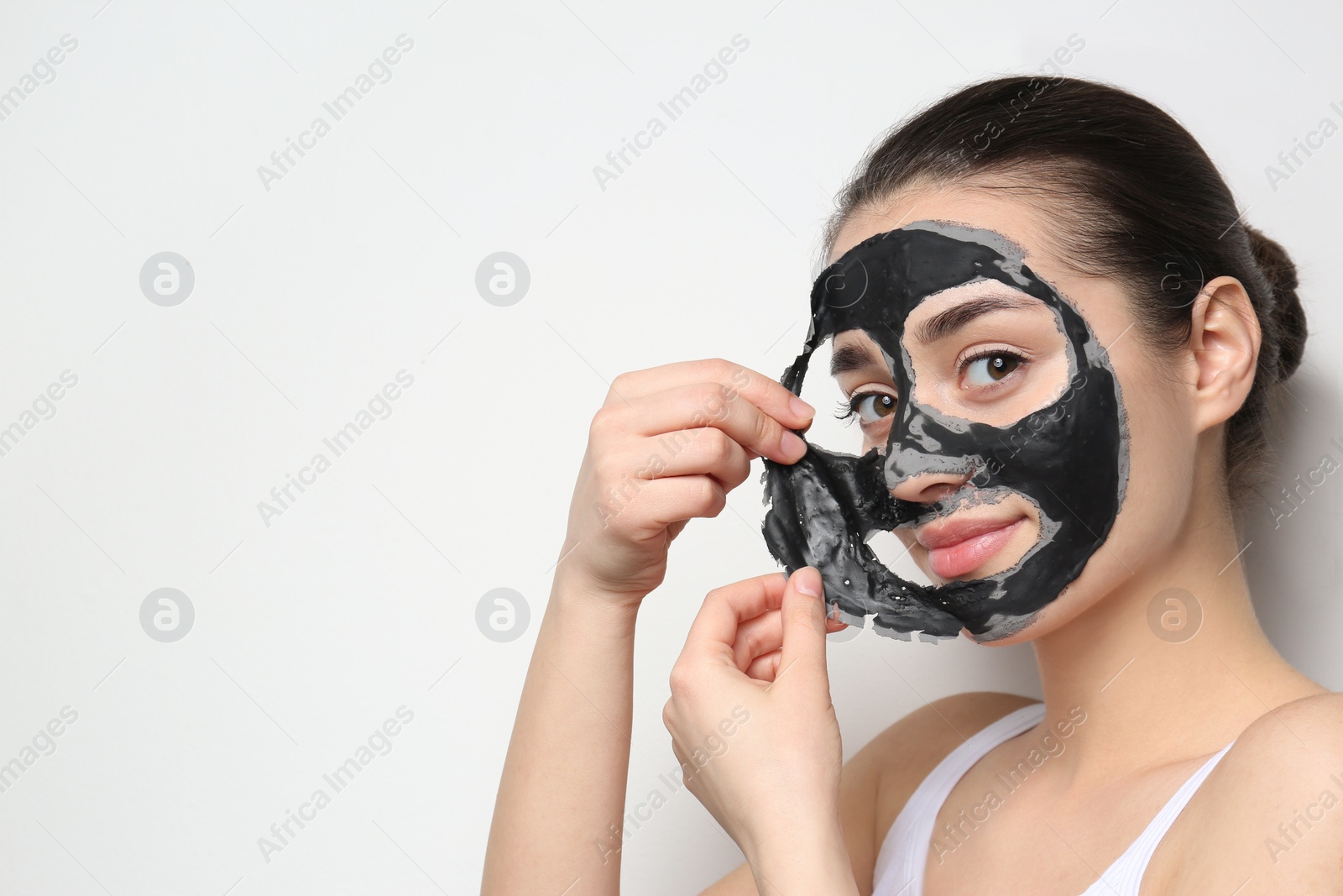 Photo of Beautiful young woman removing black mask from her face on white background. Space for text