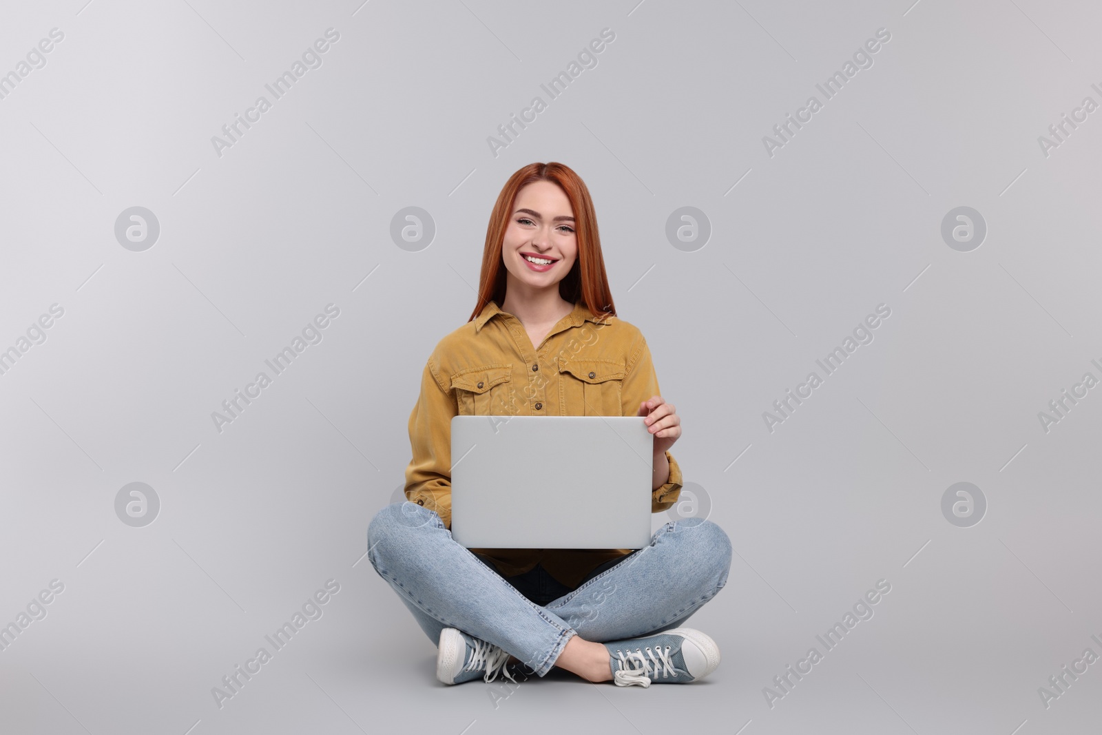 Photo of Smiling young woman with laptop on grey background