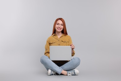 Photo of Smiling young woman with laptop on grey background