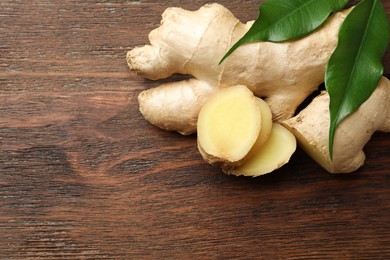 Photo of Cut and whole fresh ginger with leaves on wooden table, top view. Space for text