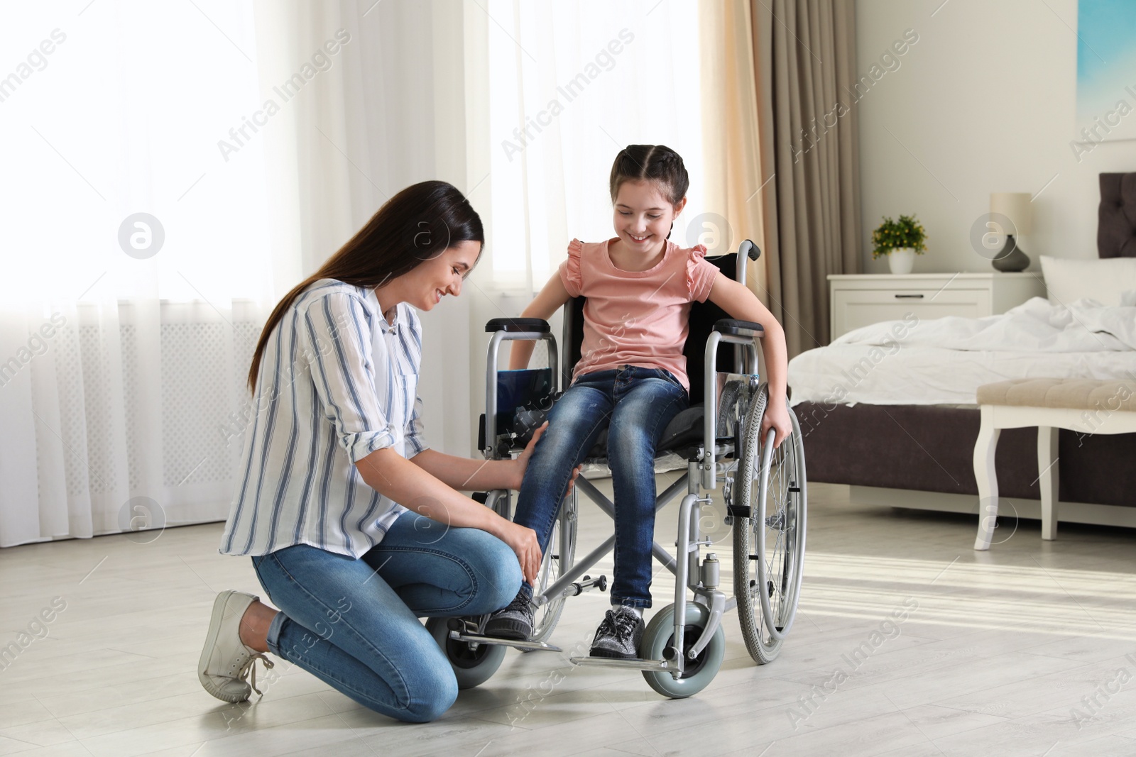 Photo of Young woman helping her disabled daughter get in wheelchair at home