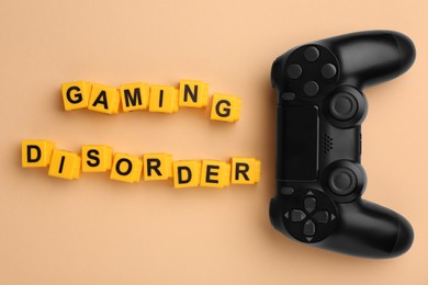 Photo of Phrase Gaming Disorder made of yellow cubes and gamepad on beige background, flat lay. Addictive behavior